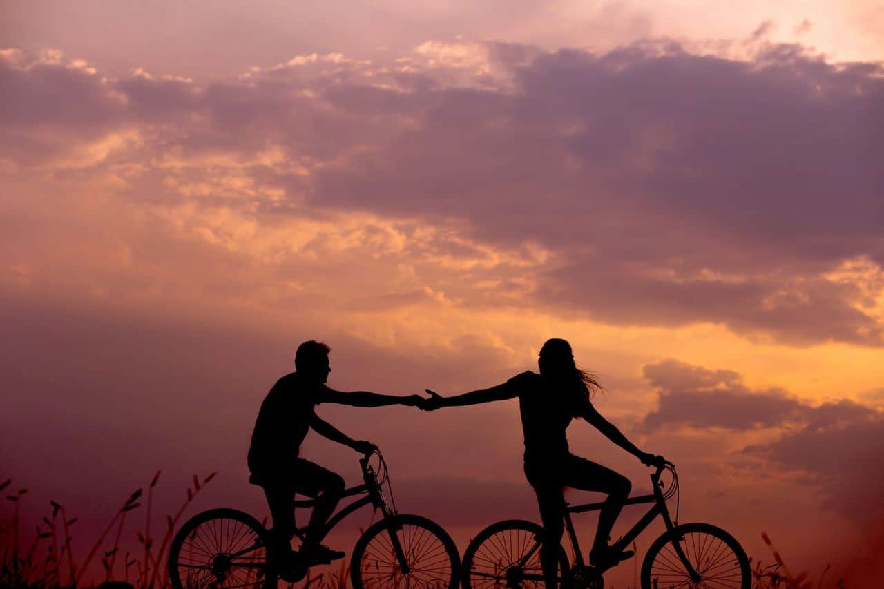 Photo of two people cycling and reaching for one another